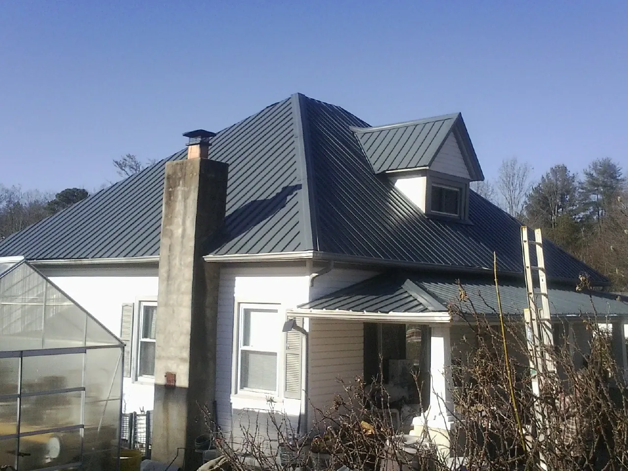 Dark blue standing seam metal roof on a white farmhouse with dormer — Slate & Tile Roof Repair by Roofing Brothers in Flanagan