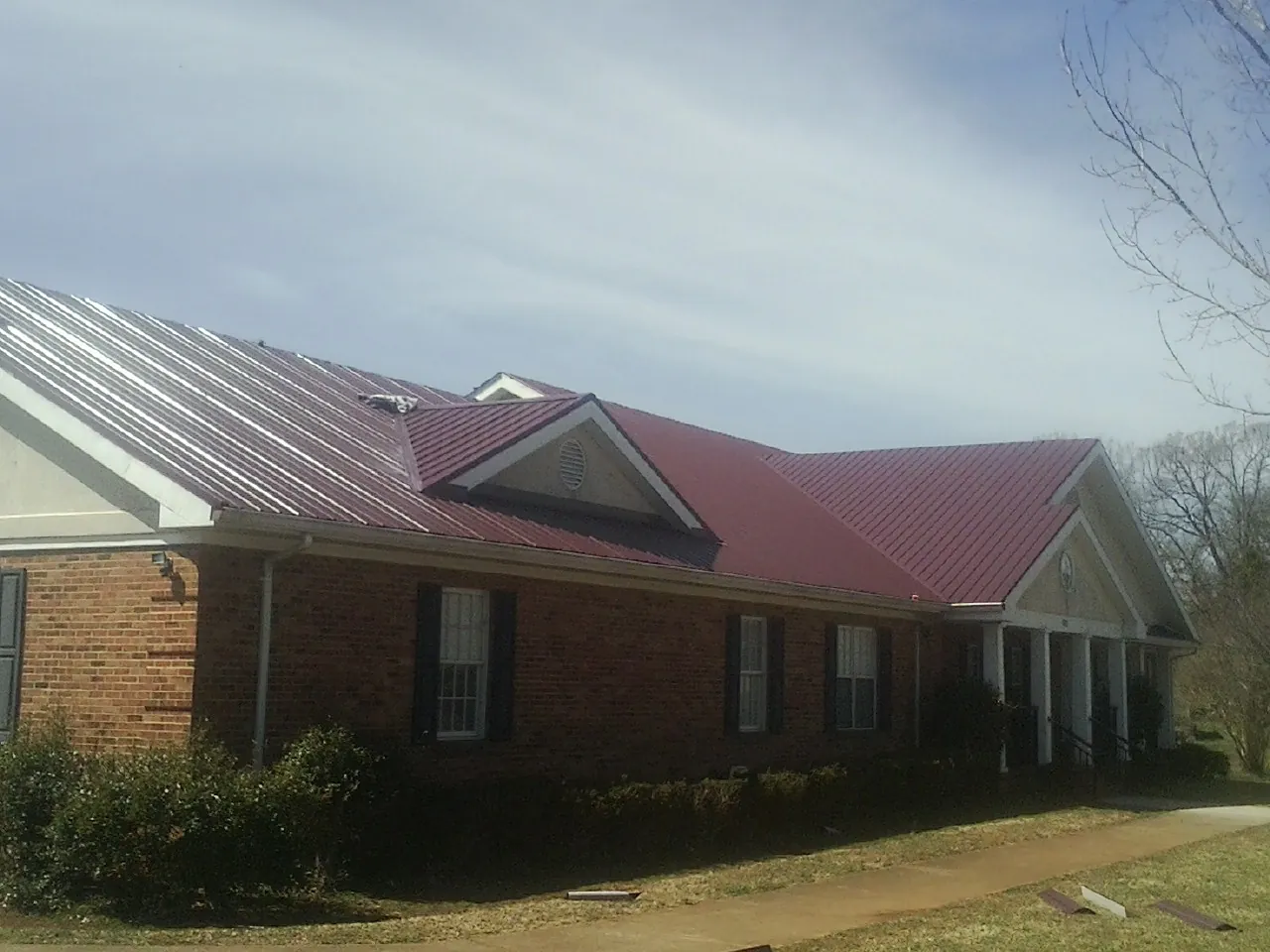Red metal roof with gabled entries on a long brick building, from a Hail Damage Roof Repair job in Flanagan