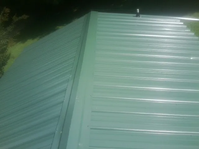 New green metal panels meeting at the ridge of a roof — Flat Roof Repair work by our crew in Flanagan
