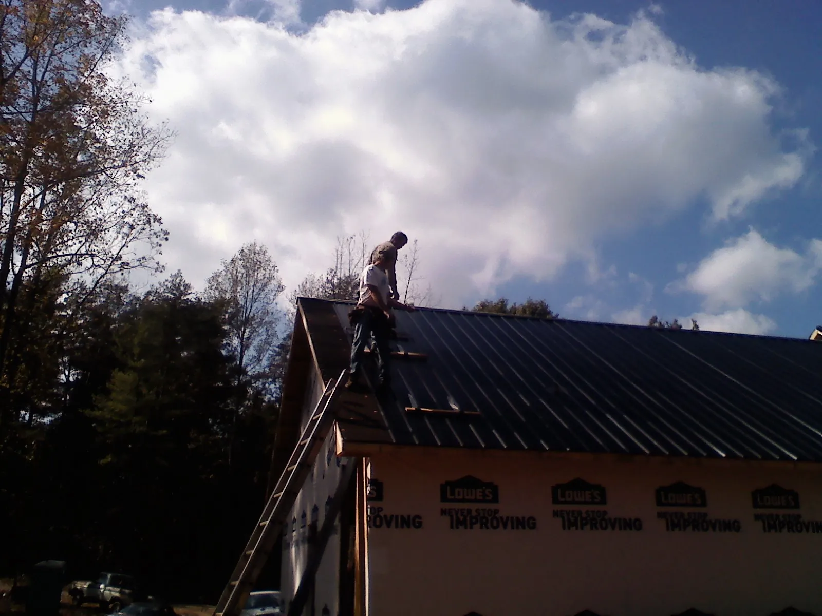 Roofer fastening dark metal panels high against a cloudy sky, from a Roof Inspection job in Flanagan