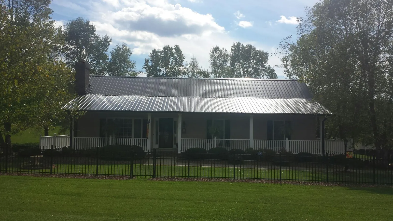 Gray metal roof on a brick ranch with a full width front porch — Gutter Guard Installation work by our crew in Flanagan