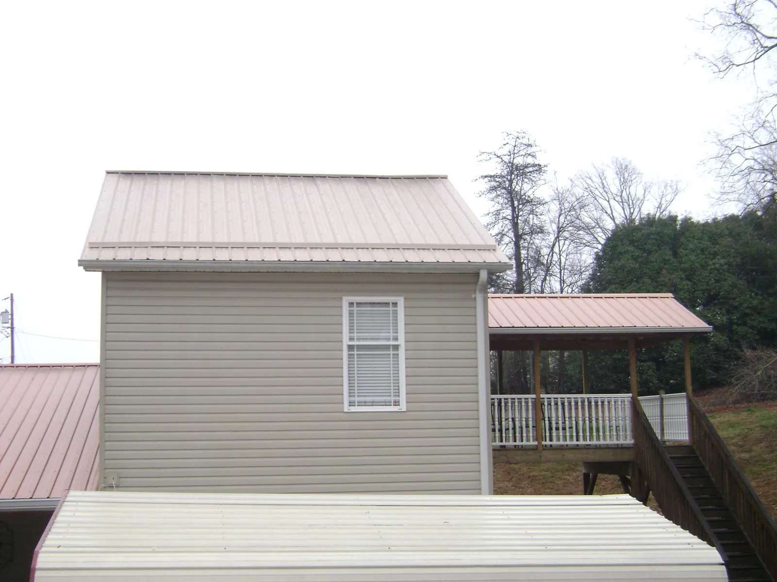 Tan metal roofs on a two story addition and attached porch, from a Roof Replacement job in Flanagan